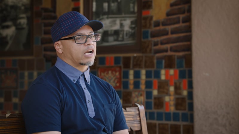 A man in blue shirt and hat sitting down.