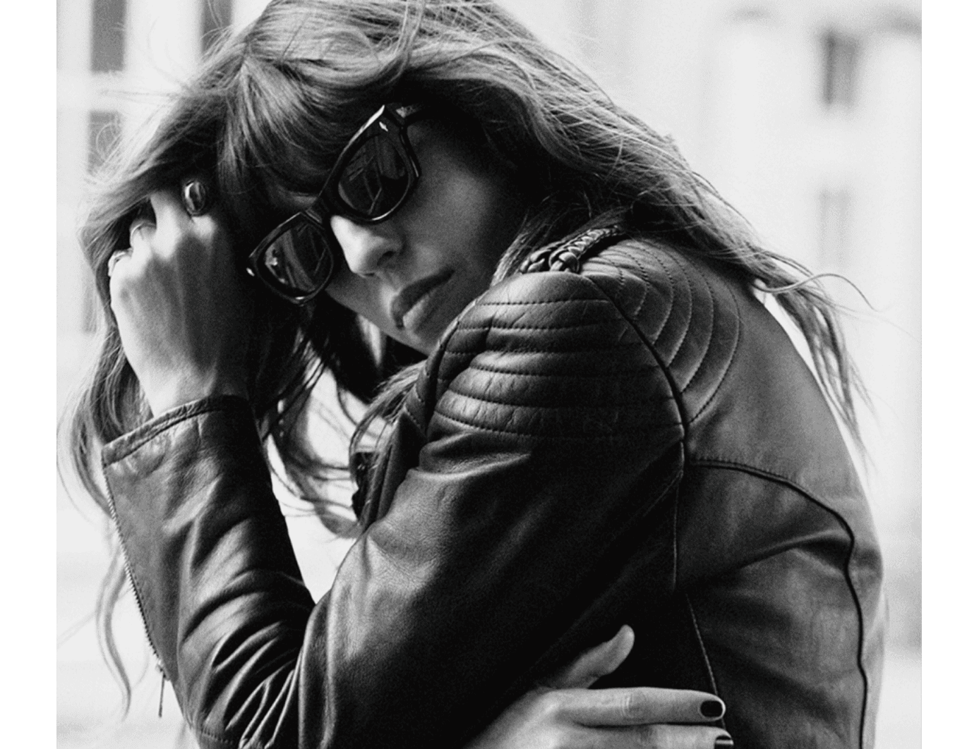 A woman in sunglasses and leather jacket touching her hair.